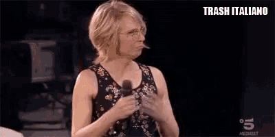 a woman in a tank top and glasses is holding a microphone and making a funny face .