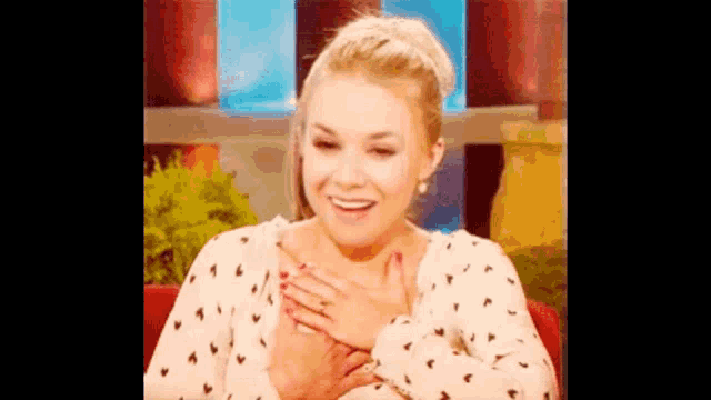 a woman is sitting on a red couch with her hands on her chest and smiling .