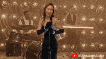 a woman singing into a microphone in front of a drum set and a youtube logo