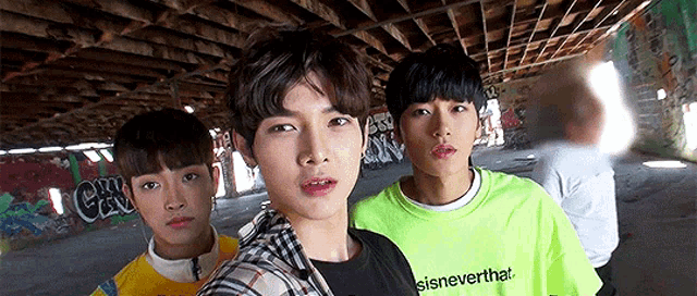 three young men are standing next to each other in a room with graffiti on the wall .