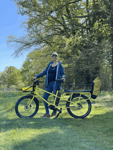 a woman stands next to a yellow bike in a field