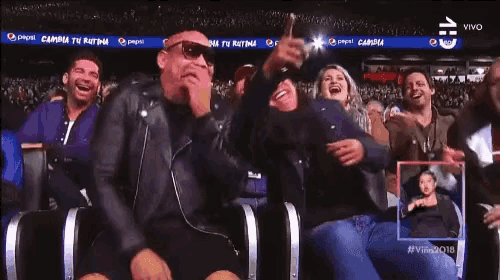a group of people laughing in a stadium with a pepsi banner behind them