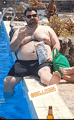a man is sitting on the edge of a swimming pool with a bag of doritos on his stomach