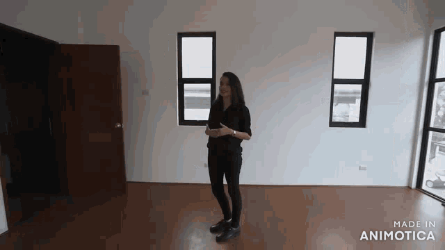 a woman in a black shirt is standing in a room with two windows .