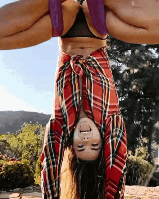 a woman in a plaid shirt is upside down and smiling