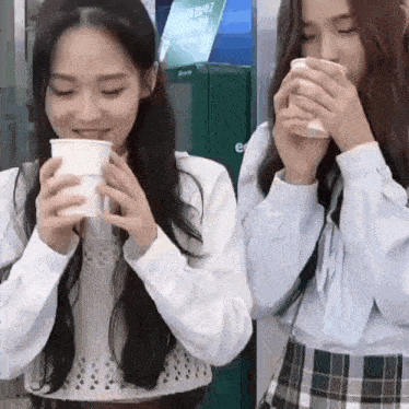 two girls are drinking coffee from paper cups while standing next to each other .