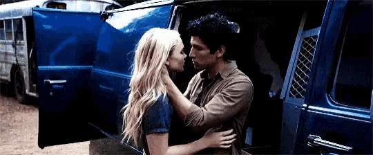 a man and a woman are hugging and kissing in the back of a blue van .