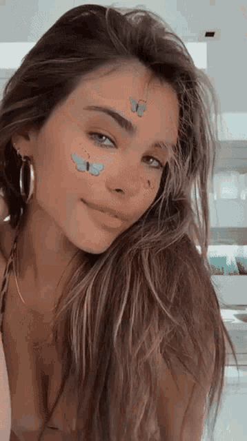 a woman with butterfly stickers on her face looks at the camera