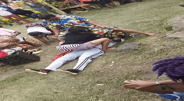 a group of people laying on top of each other in the grass .