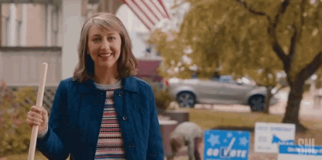 a woman is standing in front of a sign that says `` go vote '' holding a broom .