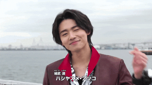 a young man in a red jacket is smiling in front of the ocean