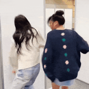two women are standing next to each other in front of a white wall .