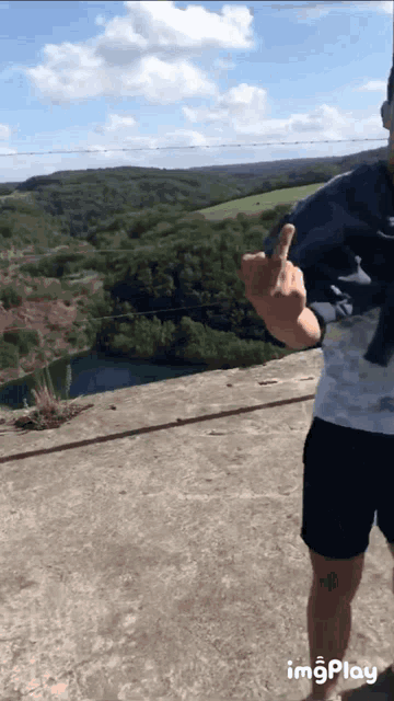 a man is giving the middle finger in front of a lake and mountains