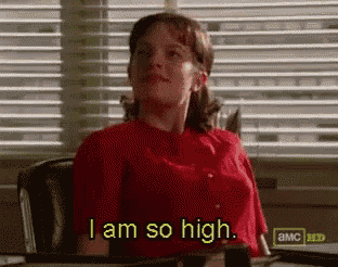 a woman in a red shirt is sitting at a desk and saying i am so high .