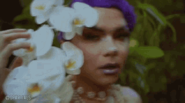 a woman with purple hair is holding white orchids in her hands .