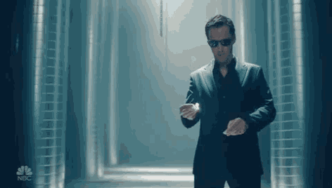 a man in a suit and sunglasses is standing in a hallway with a nbc logo on the bottom