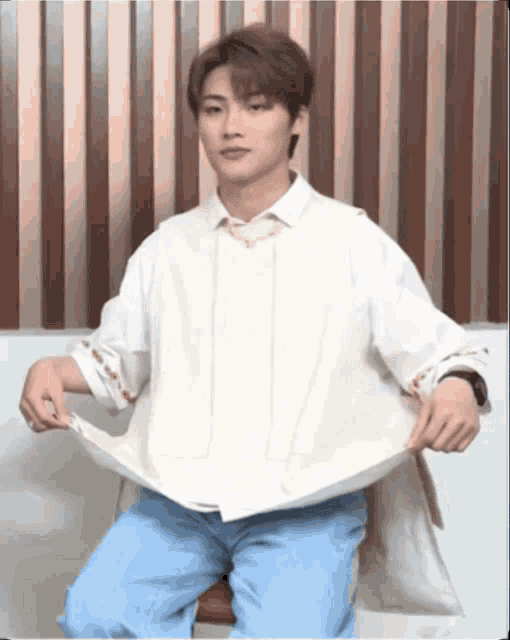 a young man wearing a white shirt and blue jeans is sitting on a couch
