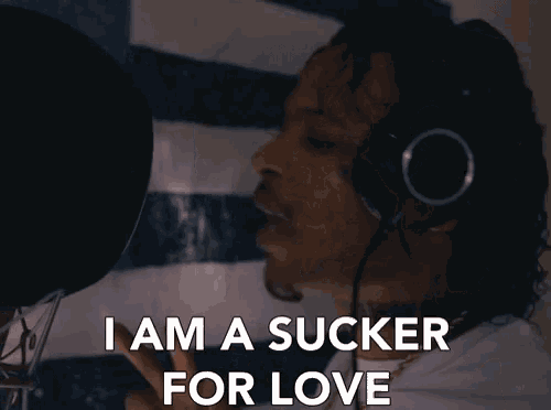 a man singing into a microphone with the words i am a sucker for love behind him