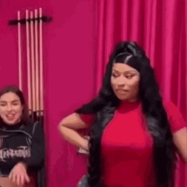 a woman in a red shirt is standing next to a woman in a black shirt in front of a pink curtain .