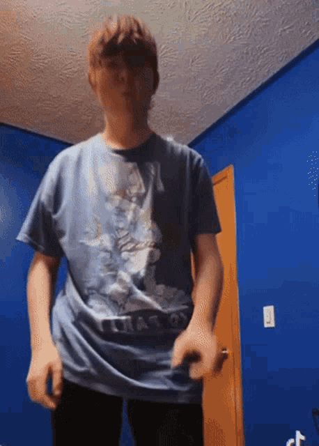 a boy wearing a blue t-shirt with a dragon on it is standing in front of a blue wall