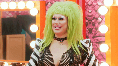 a woman with green hair is smiling in front of a mirror with lights