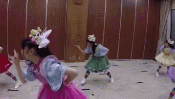 a group of girls are dancing in a room with a wooden wall in the background .