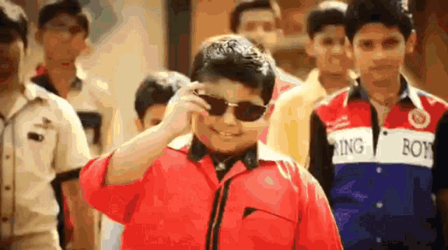 a boy wearing sunglasses stands in front of a group of boys wearing shirts that say ring