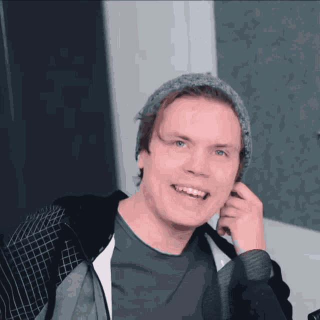 a man wearing a beanie and a hoodie smiles