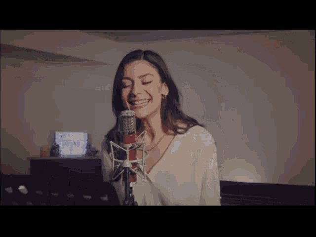a woman singing into a microphone with a sign in the background that says " welcome sound "