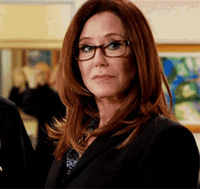 a woman wearing glasses and a suit looks at the camera