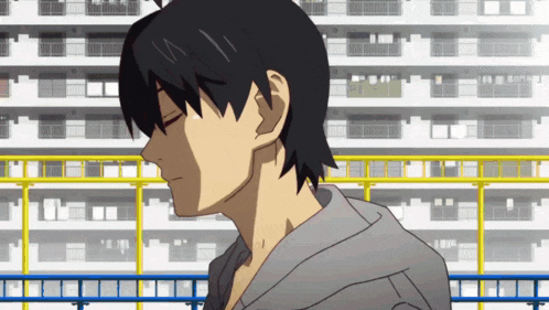 a man in a grey hoodie stands in front of a building with his eyes closed