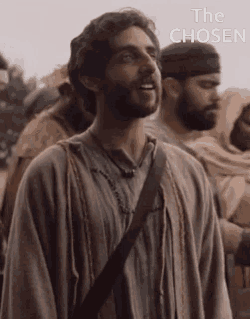 a man with a beard is standing in front of a crowd with the words the chosen above him .