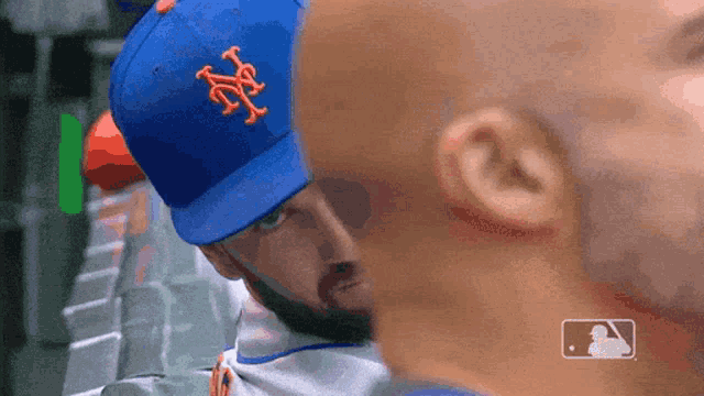 a man wearing a new york mets hat looks at another man