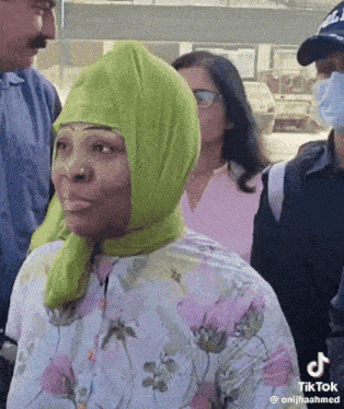 a woman wearing a green scarf on her head is standing in a crowd of people .