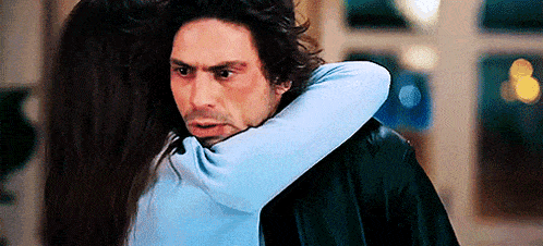 a man and a woman are hugging each other in a room . the woman is wearing a blue sweater .