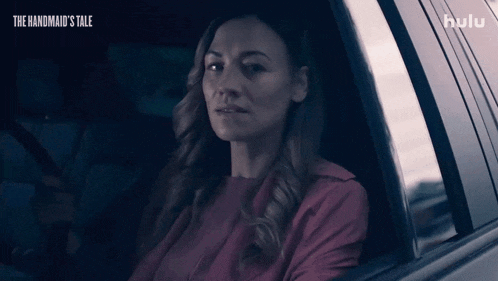 a woman is sitting in a car with the handmaid 's tale on the bottom