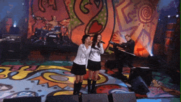 two girls singing on a stage with a nbc logo in the background