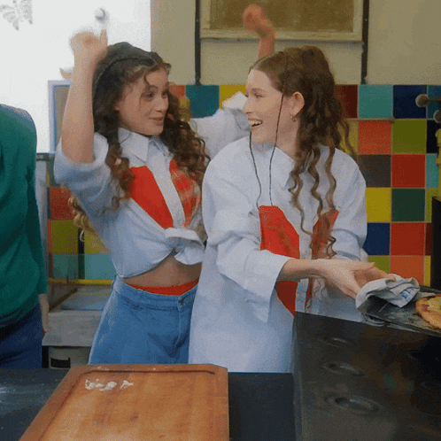two girls are standing next to each other in a kitchen with their arms in the air
