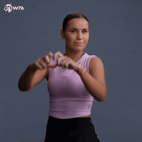 a woman in a purple tank top making a heart shape with her hands .