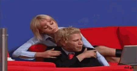 a woman is sitting on a man 's back in a red chair with a laptop .