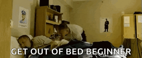two men are sleeping in a dorm room with the words `` get out of bed beginner '' .