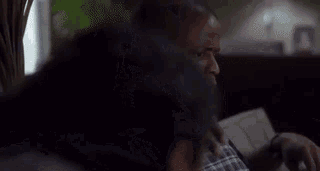 a man is sitting on a couch talking on a cell phone while a woman looks on .