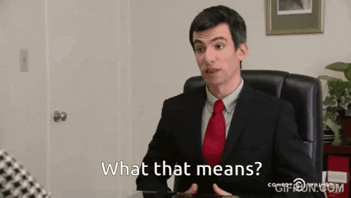 a man in a suit and tie is sitting at a desk and says what that means