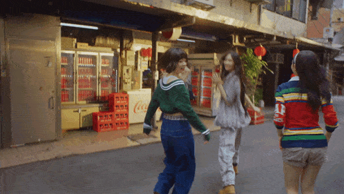 three women are walking down a street in front of a coca cola cooler