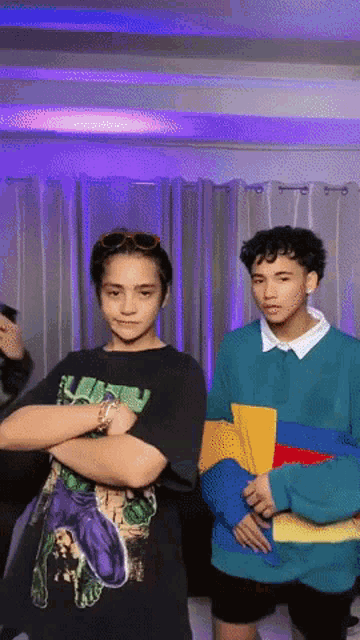 two young men are standing next to each other with their arms crossed in front of a purple curtain .