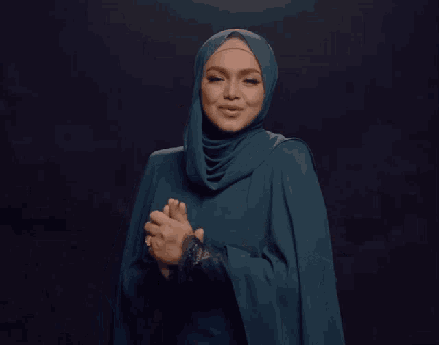a woman wearing a hijab is smiling with her hands on her face