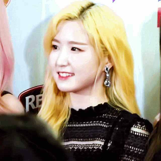a woman with blonde hair is smiling in front of a sign that says re.