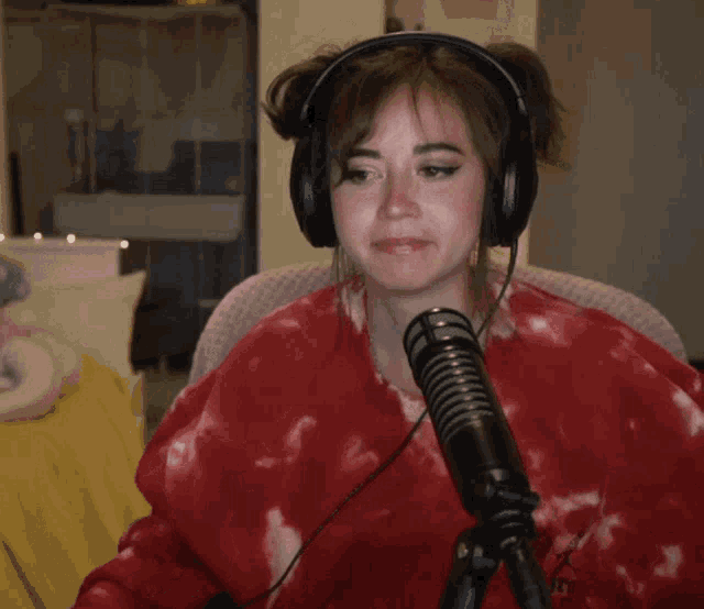 a woman wearing headphones is sitting in front of a microphone with a red tie dye shirt on