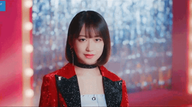 a woman wearing a red jacket and a black choker looks at the camera