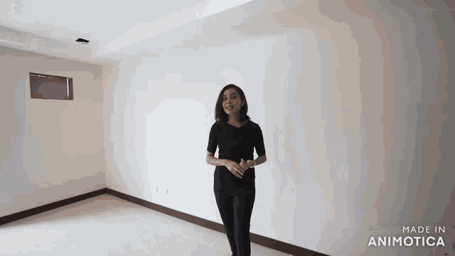 a woman in a black shirt and black pants is standing in an empty room with white walls .